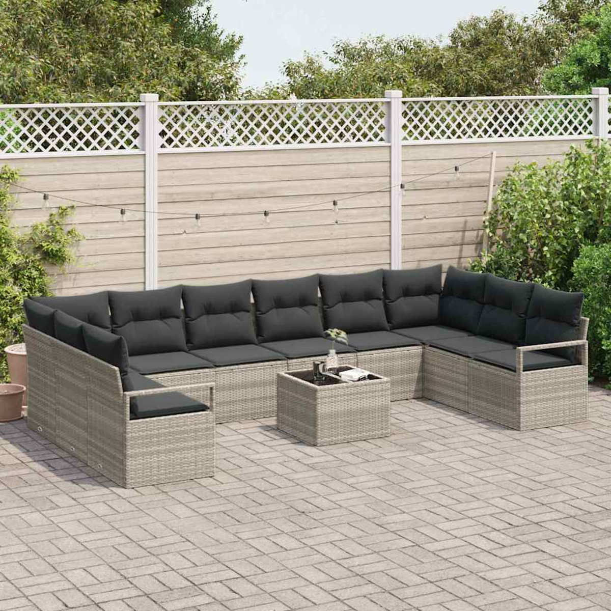 Garten-Terrassenset mit grauen Kissen auf hellem Korbgeflecht. Davor ein kleiner quadratischer Tisch. Im Hintergrund ein weißer Zaun und Grün.