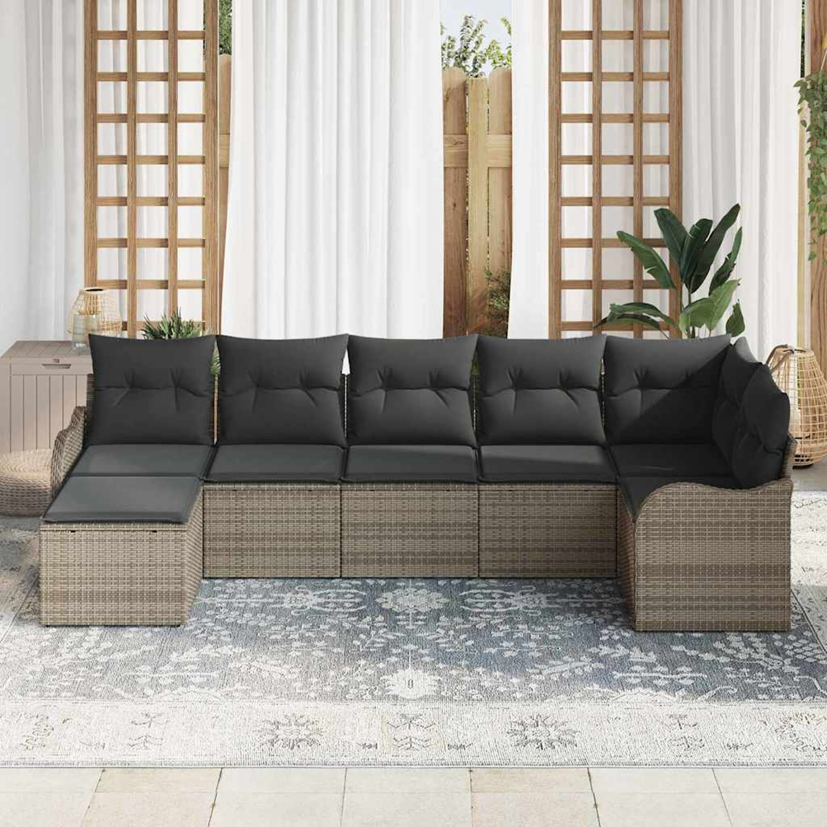 Ein Ecksofa im Freien mit grauen Kissen auf einem gemusterten Teppich, in der Nähe eines Fensters mit weißen Vorhängen.