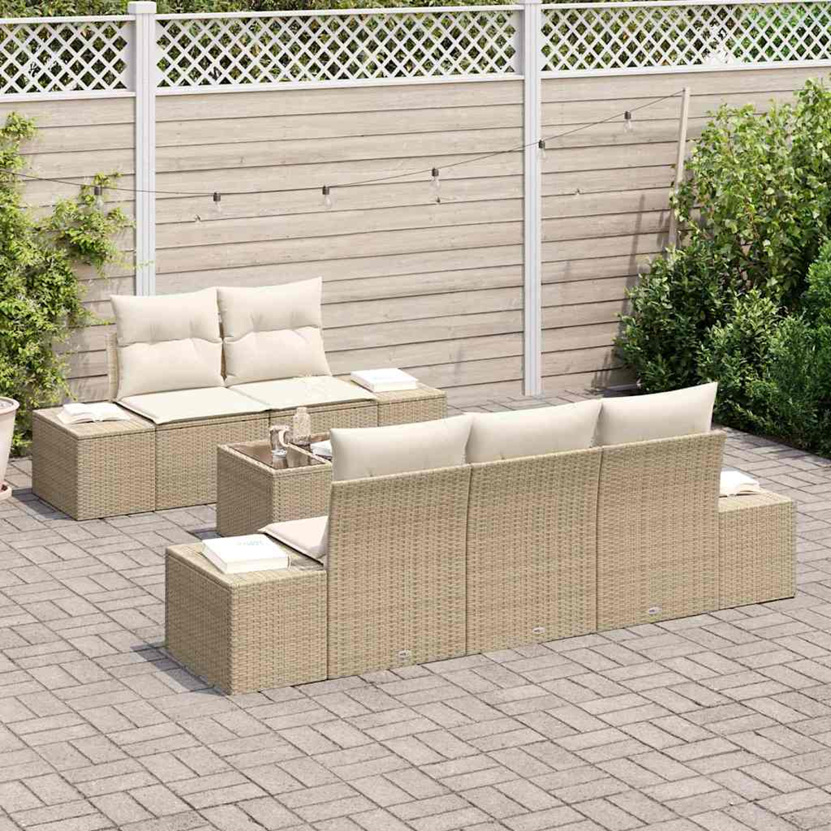 Juego de patio al aire libre con muebles de mimbre beige, cojines crema y mesa de centro de vidrio. Contra valla de madera y vegetación.