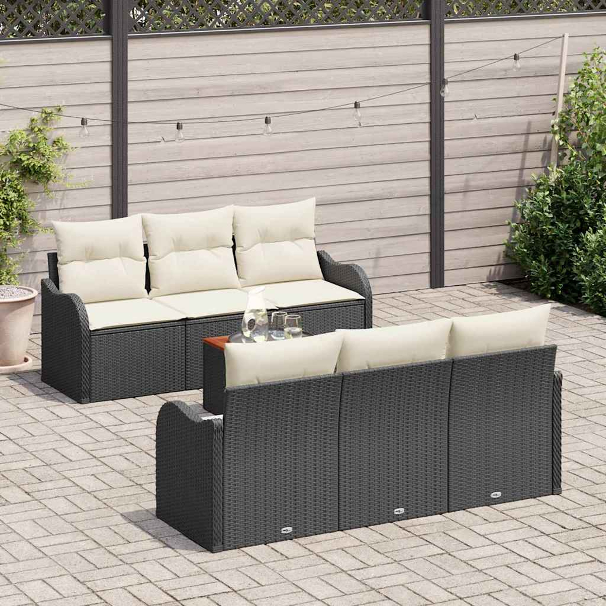 Escena al aire libre con sofás de ratán gris oscuro con cojines crema. Una pequeña mesa con vasos está entre los sofás. Luces de cadena arriba.