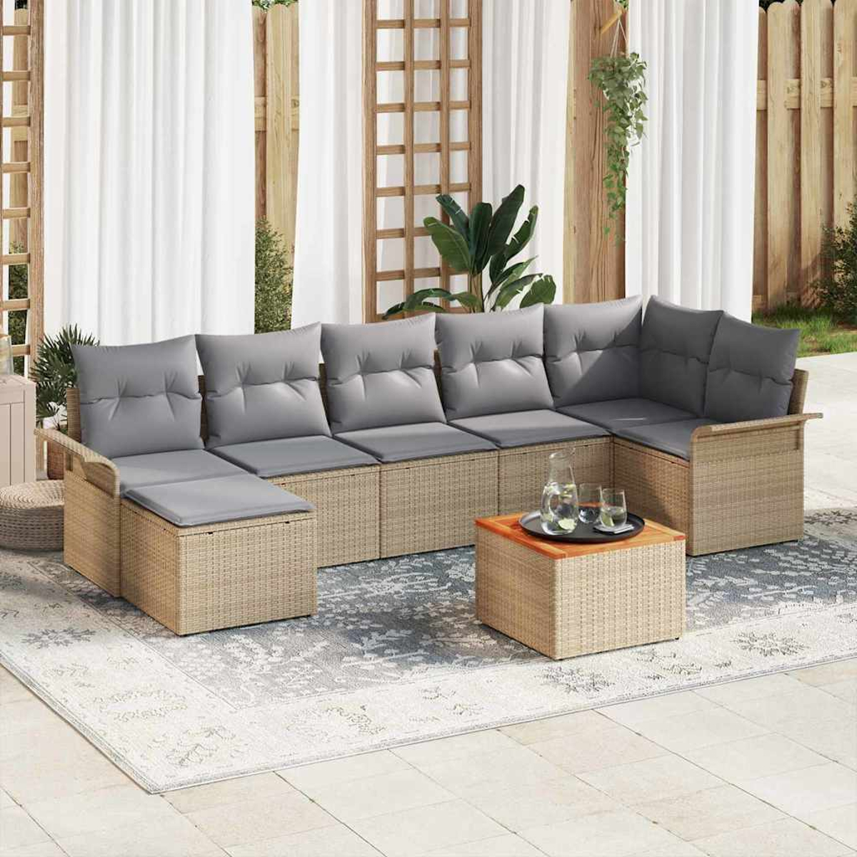 Outdoor-Ecksofa mit grauen Kissen auf einem gemusterten Teppich. Ein kleiner Tisch hält Getränke. Holzzaun und weiße Vorhänge im Hintergrund.