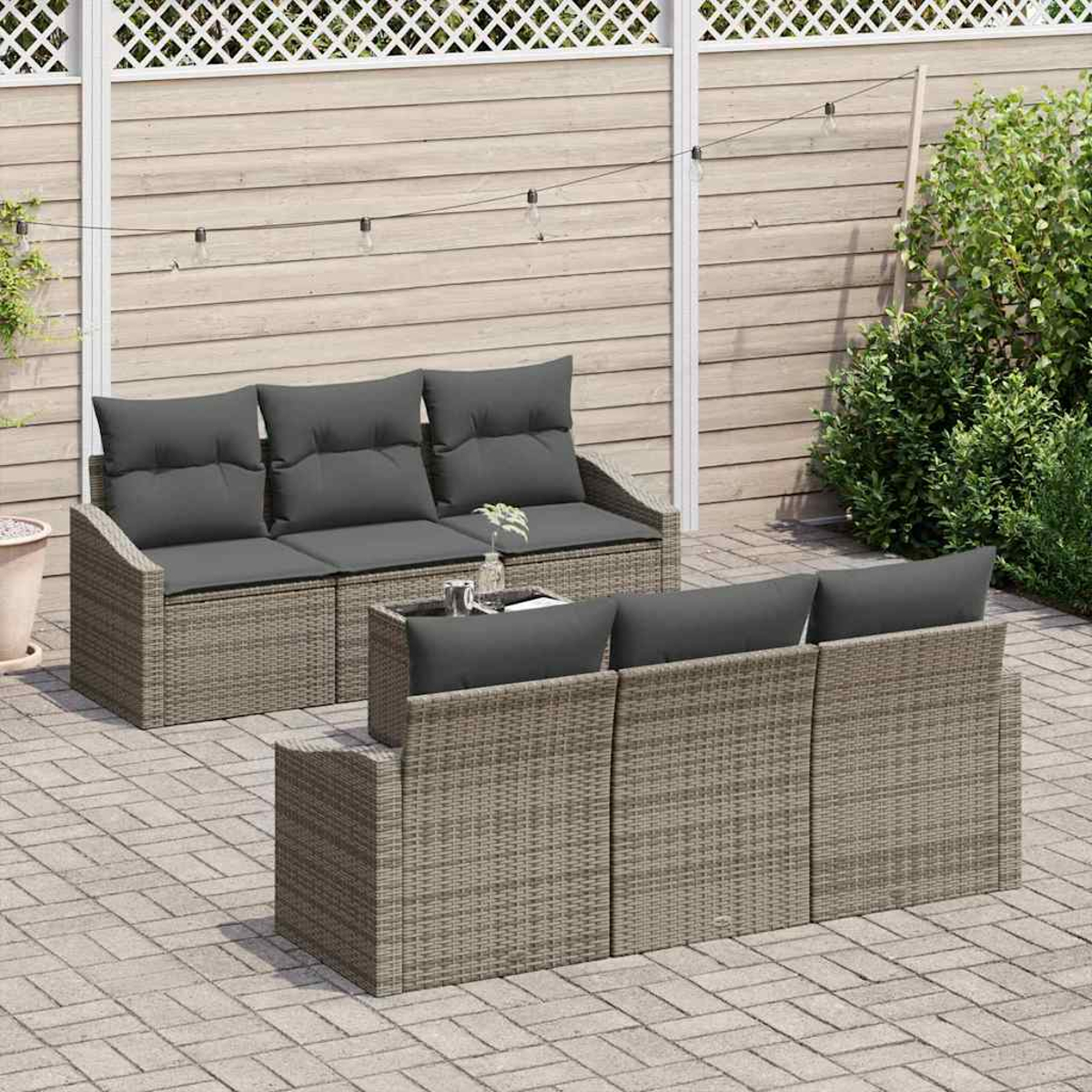 Gartenmöbel-Set mit grauen Kissen. Im Hintergrund ein Holzzaun, eine grüne Pflanze und Lichterketten.