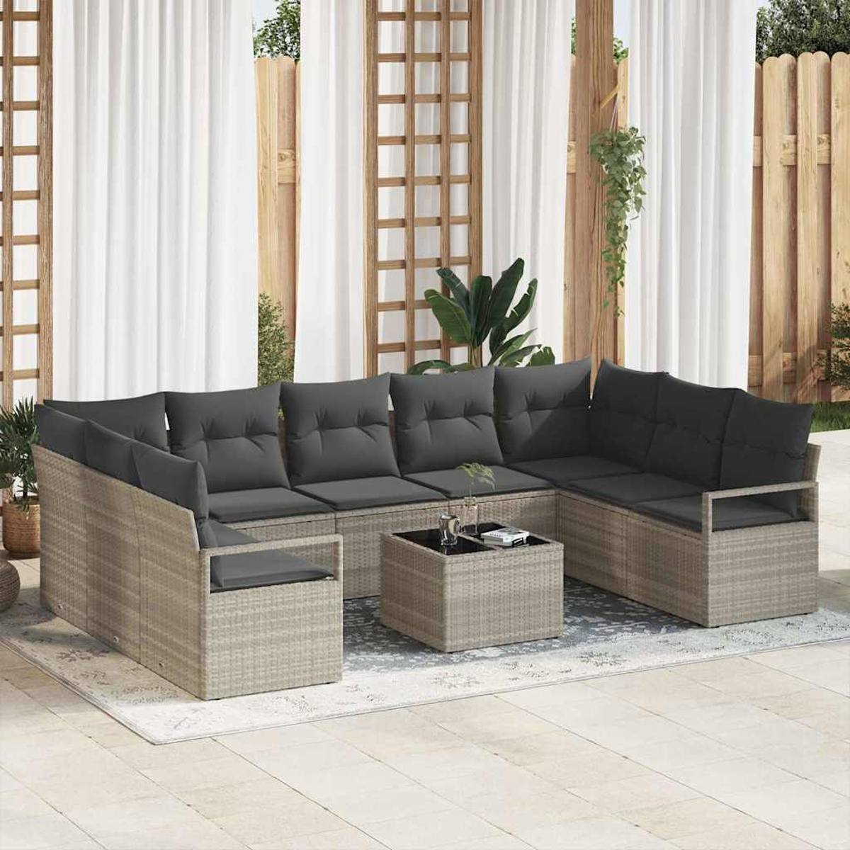 Outdoor-Sitzgruppe mit grauen Kissen. Enthält Sofa, Couchtisch und Teppich auf einer Terrasse. Vorhänge und Holzzaun im Hintergrund.