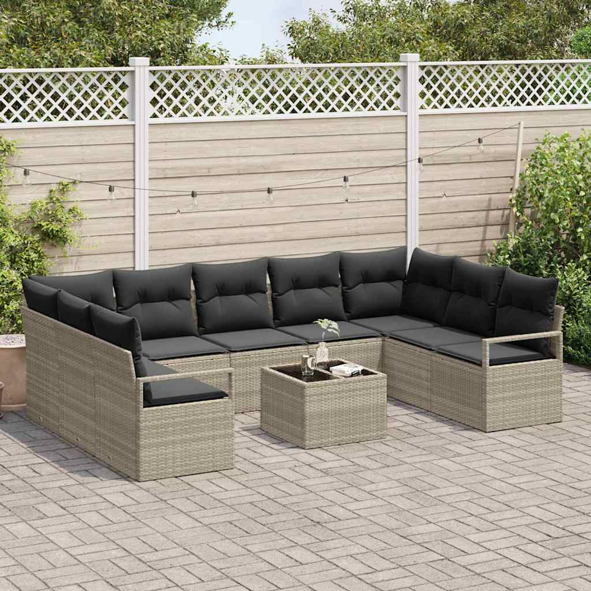 Ein Ecksofa im Freien mit schwarzen Kissen und einem kleinen Tisch. Im Hintergrund befinden sich ein Zaun und Grün, mit Lichterketten.