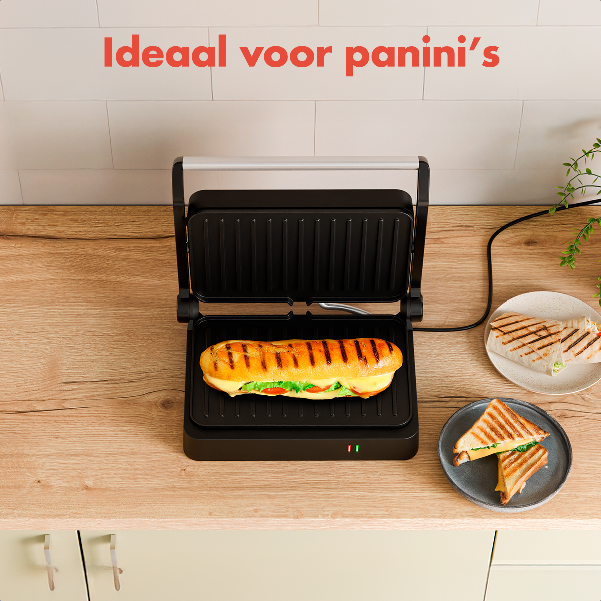 A panini press with a sandwich inside. Two plates with sandwiches and a wrap are also on the wooden counter. Text says 'Ideal for panini's'.