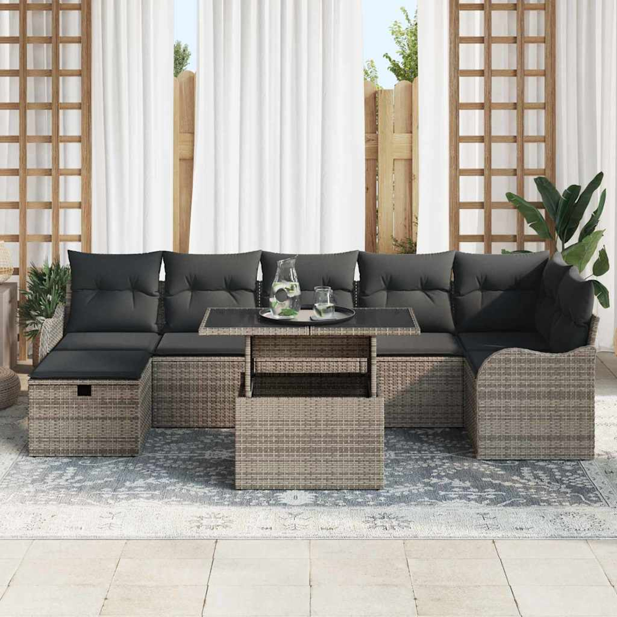 Outdoor-Sofa aus Korbgeflecht mit grauen Kissen, Couchtisch, Glas Wasser. Weiße Vorhänge im Hintergrund.