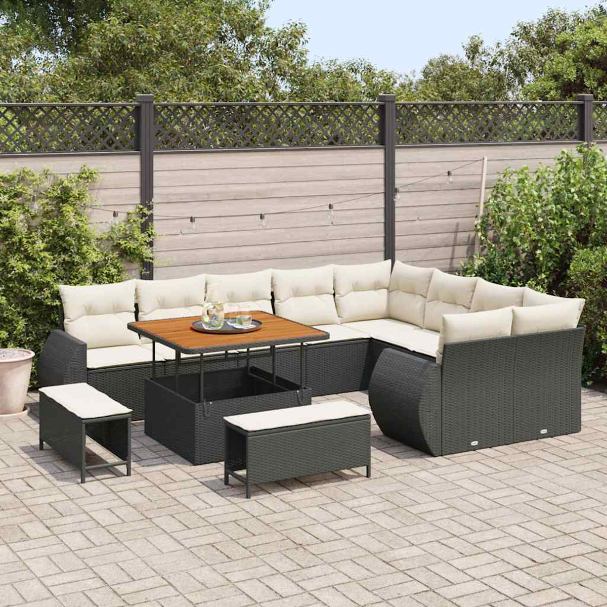 Outdoor-Ecksofa mit Holztisch, Bank und Stauraumbank auf einer Backstein-Terrasse. Ein Zaun und Grün im Hintergrund.