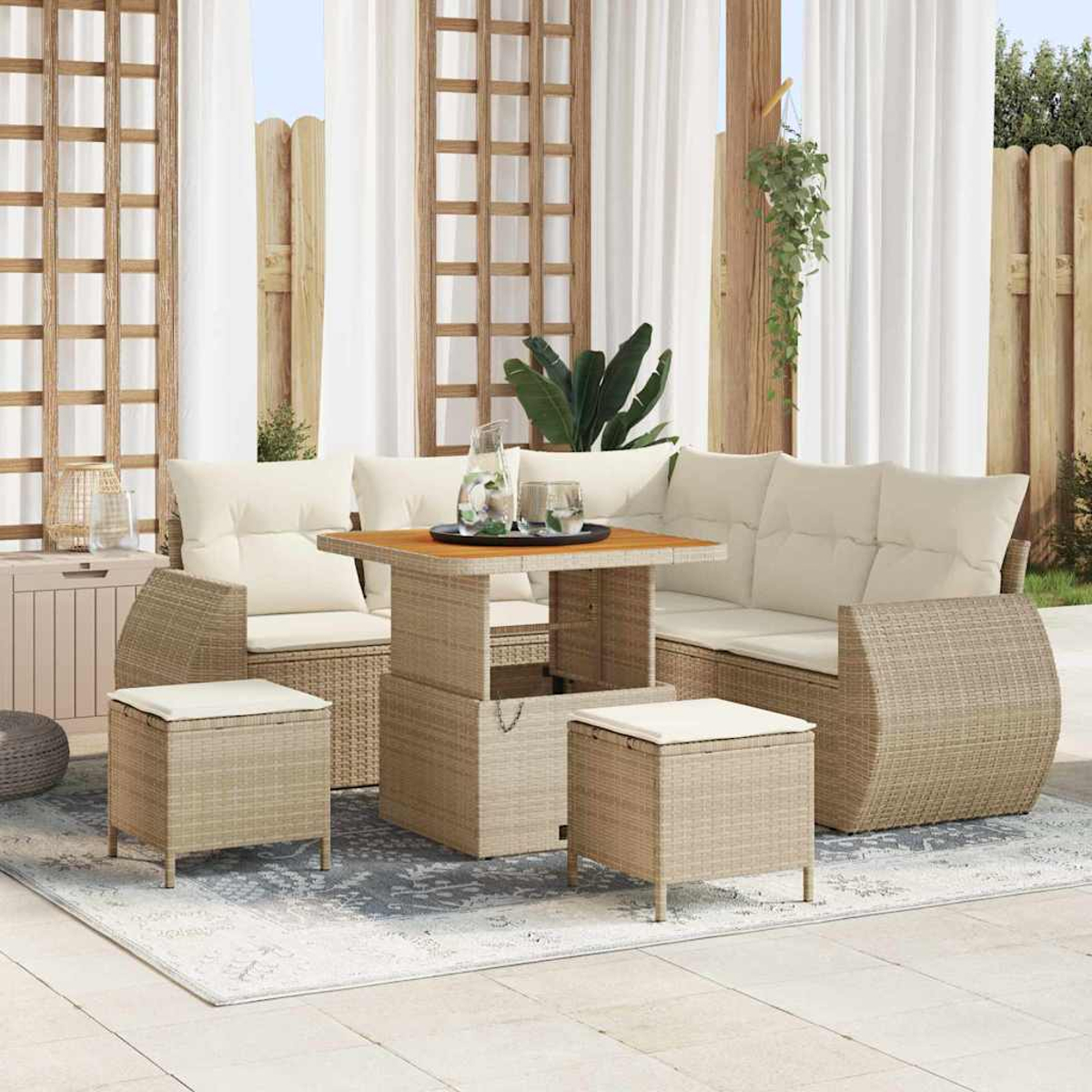Gartenmöbel-Set aus Weidengeflecht. Sofa, Stühle, Hocker und Tisch. Beige Kissen. Weiße Vorhänge und Holzgitter im Hintergrund.
