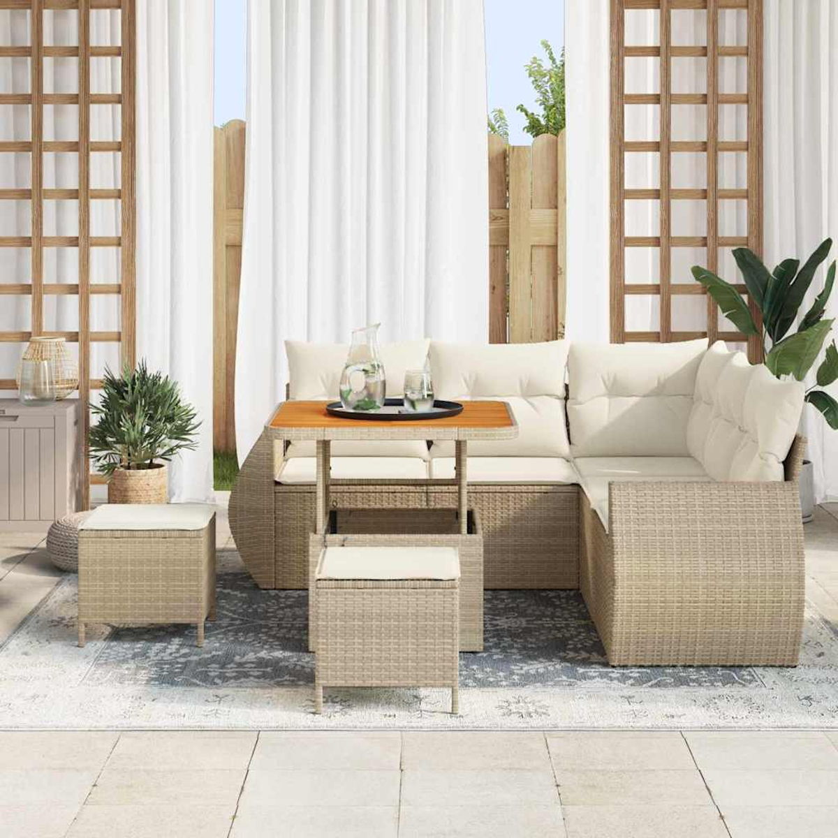 Terrassen-Set mit Korbsofa, kleinem Tisch mit Getränken und zwei Ottomanen. Im Hintergrund weiße Vorhänge und Holzzaun.