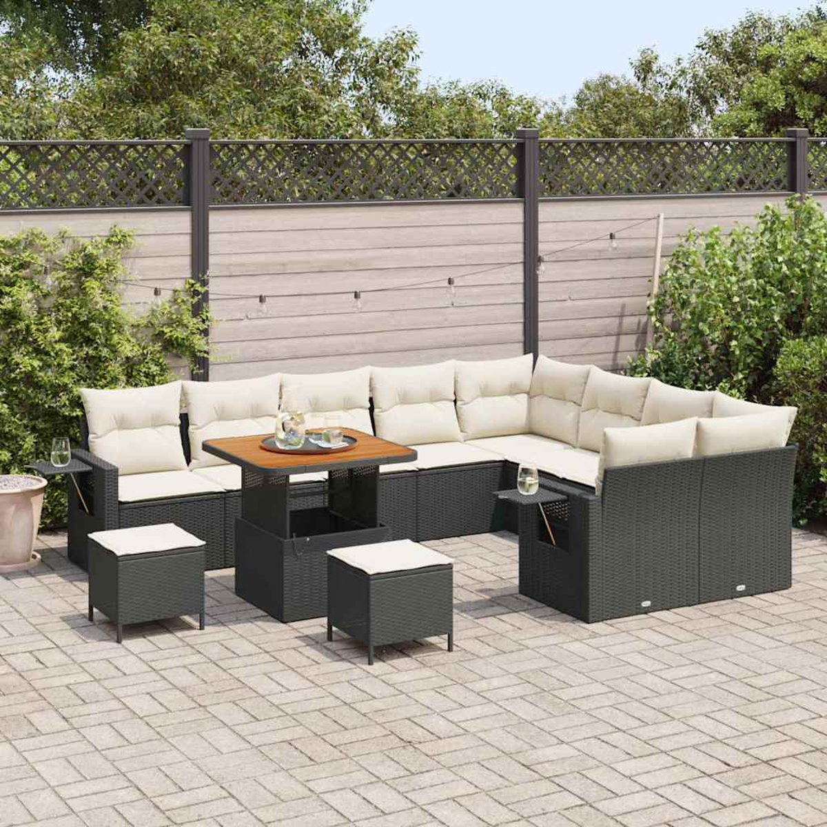 Ein Ecksofa im Freien mit beigen Kissen und einem Holztisch. Zwei Hocker stehen davor. Der Hintergrund hat einen Zaun und Grün.