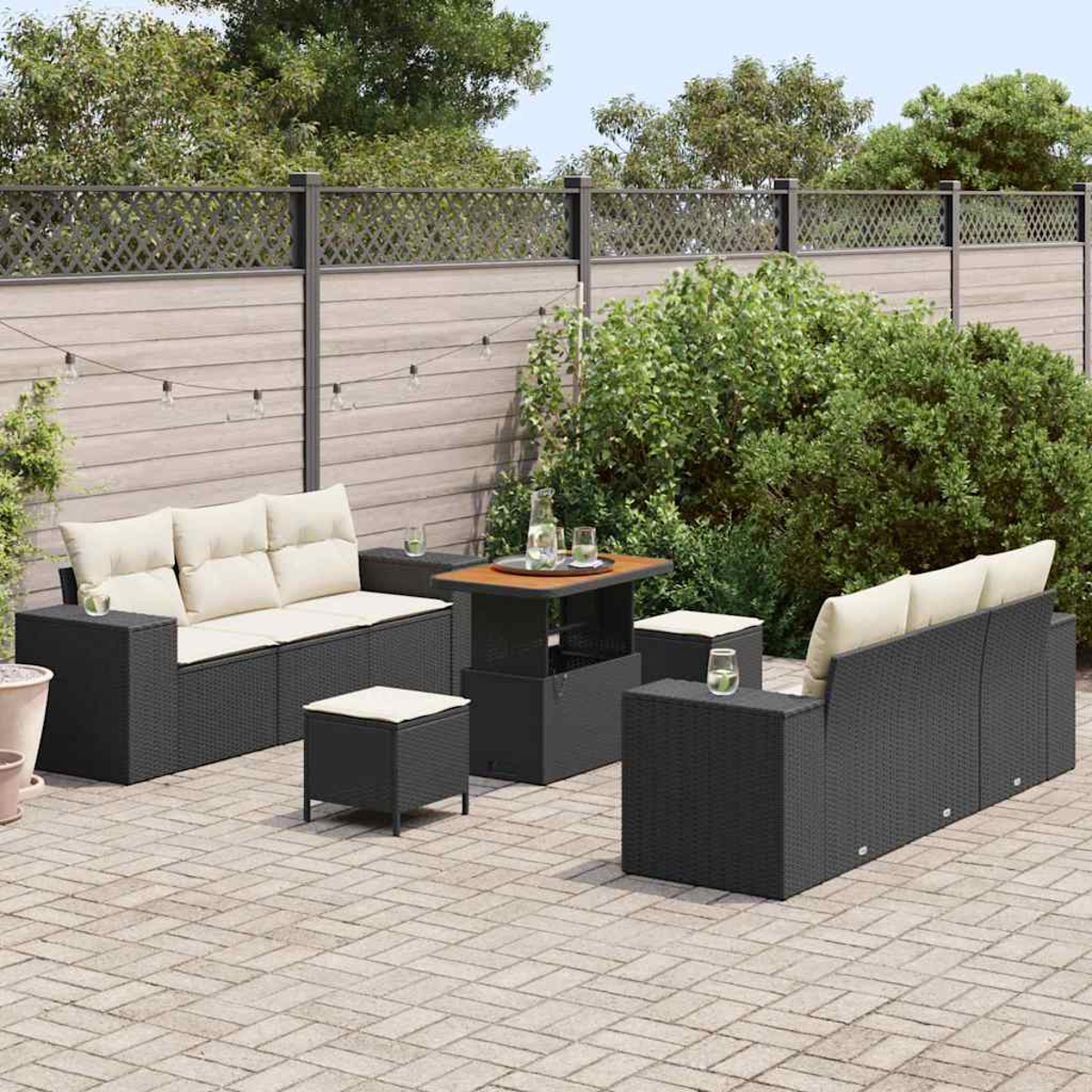 Outdoor-Terrassenset mit schwarzen Korbmöbeln und beigefarbenen Kissen. Enthält Sofas, Ottomanen und einen Tisch auf einer Ziegelterrasse mit Zaun.