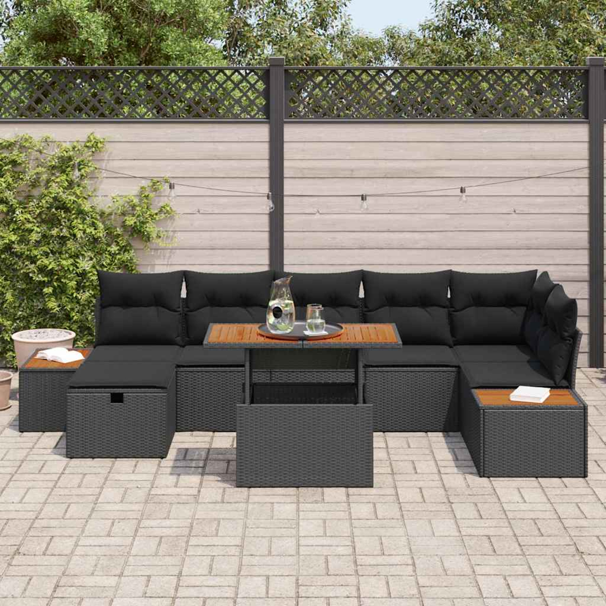 Outdoor-Ecksofa mit schwarzen Kissen, Holztisch und grauem Korbgeflecht. Auf dem Tisch stehen ein Krug und ein Glas.