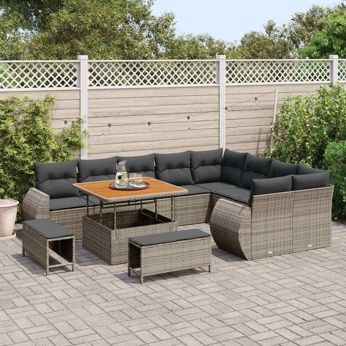 Terrassenset mit grauen Kissen und Holztisch. Enthält ein Ecksofa, Bänke und einen dekorativen Zaun im Hintergrund.