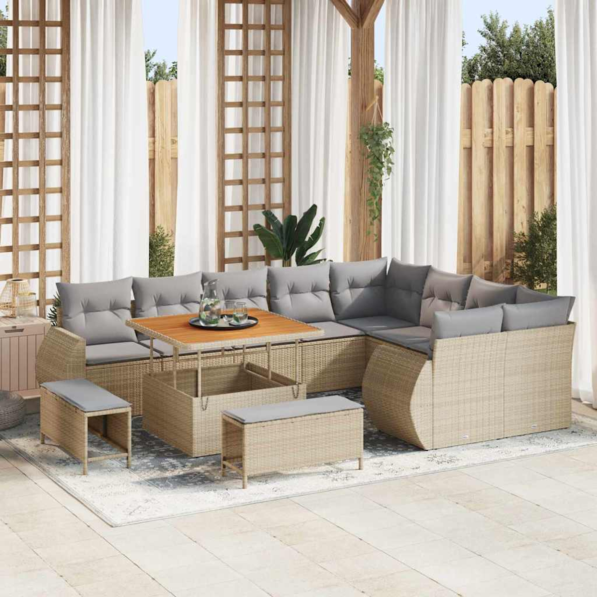 Outdoor-Rattansofa mit grauen Kissen, Holztisch und Bänken. Vorhänge und Holzzaun im Hintergrund.