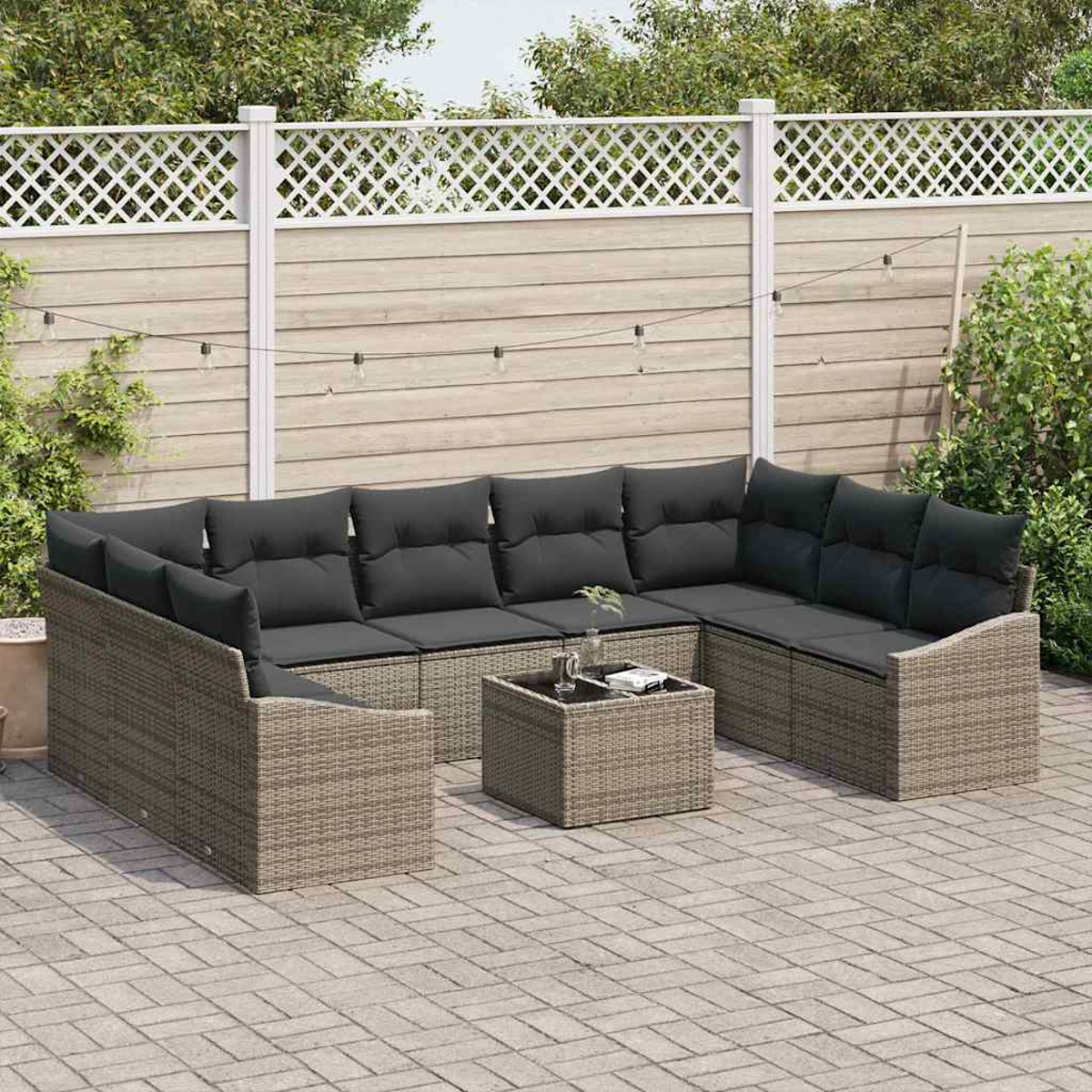 Ein Ecksofa im Freien mit grauen Kissen und einem kleinen Tisch auf einer Ziegelterrasse. Im Hintergrund ist ein weißer Zaun.