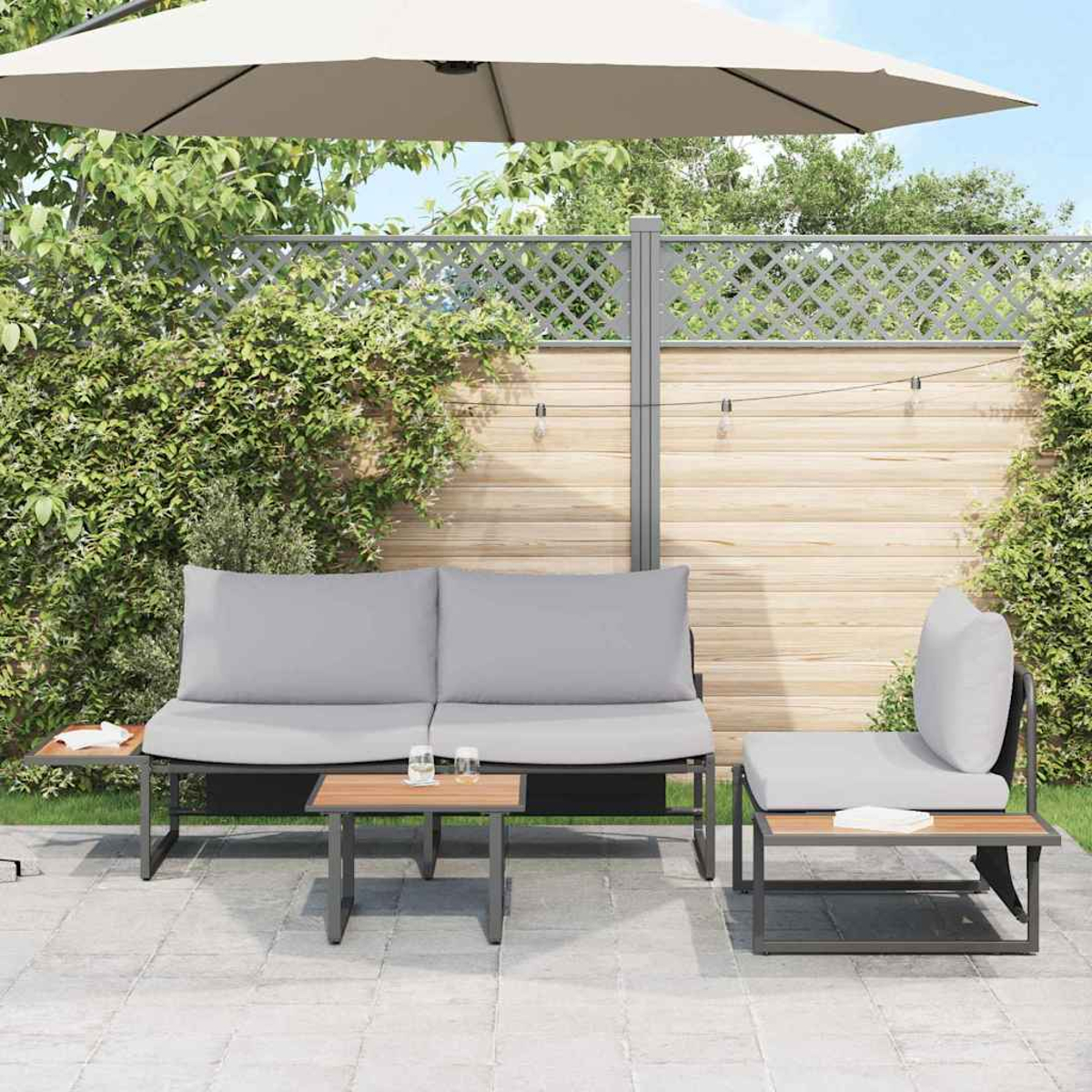 Garten-Terrassenset: graue Kissen, Holztische und ein beigefarbener Sonnenschirm, vor einem Holzzaun mit Kletterpflanzen.