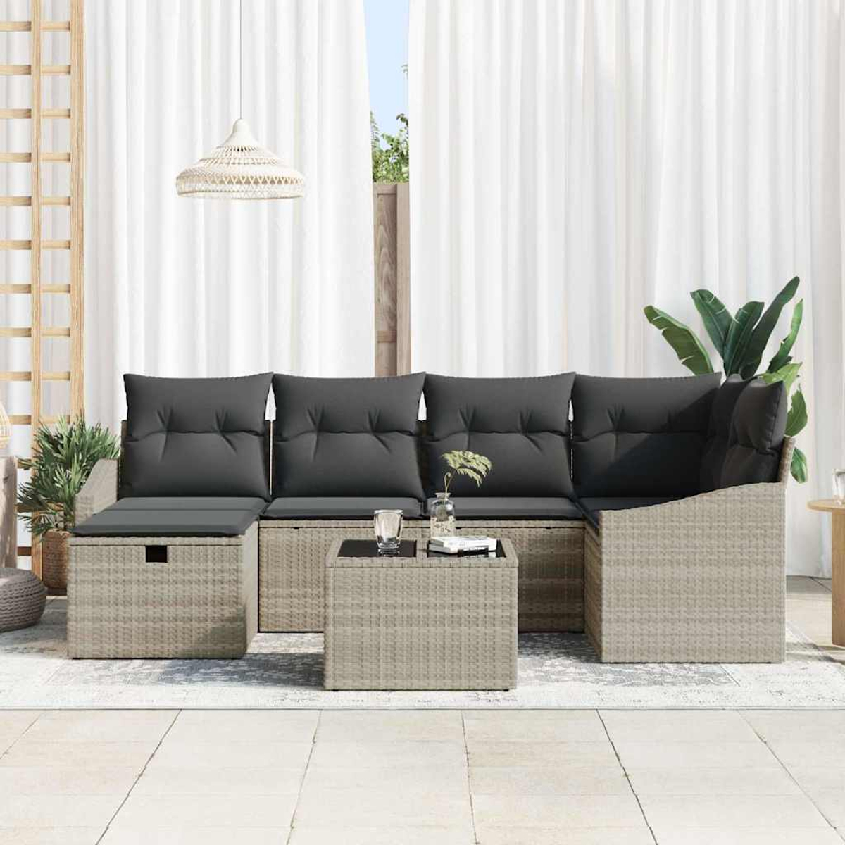 Ein Terrassenset mit grauen Kissen, einem Couchtisch und einer Hängelampe. Im Hintergrund weiße Vorhänge und grüne Pflanzen.