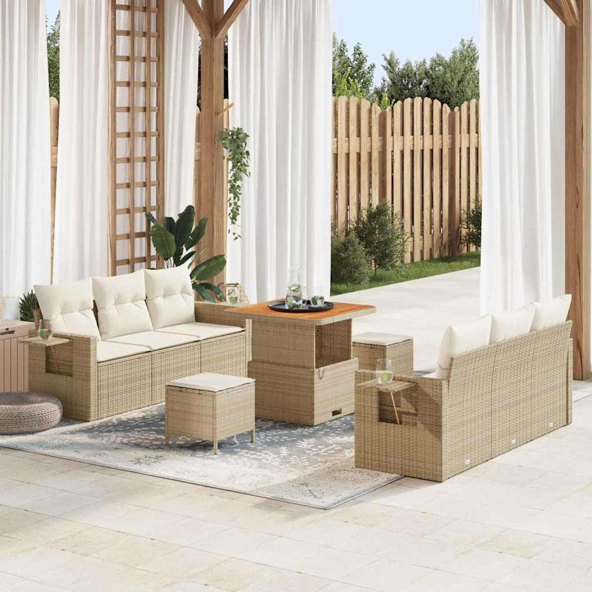 Terrassenset mit beigefarbenen Korbsesseln, Tisch und Hockern unter weißen Vorhängen. Ein Holzzaun und Grünzeug im Hintergrund.