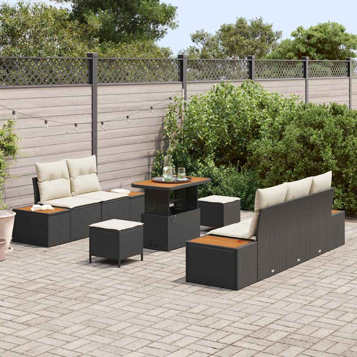 Terrassenset mit schwarzen Korbmöbeln, beigen Kissen und Holzakzenten. Enthält Sofa, Stühle und Tisch. Grünes Laub im Hintergrund.