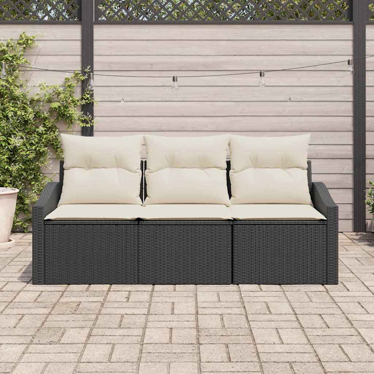Ein dunkelgraues Korbmöbel mit cremefarbenen Kissen steht auf einer Terrasse. Dahinter sind ein Holzzaun und Kletterpflanzen zu sehen.