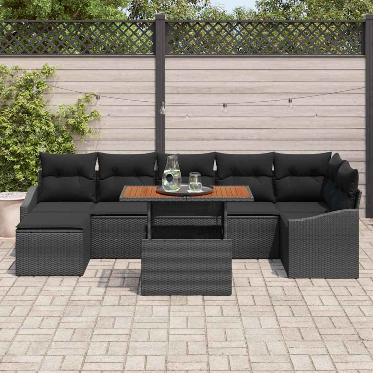 Outdoor-Ecksofa mit schwarzen Kissen und einem Holztisch. Auf dem Tisch stehen ein Glaskrug und Gläser. Pflasterung.