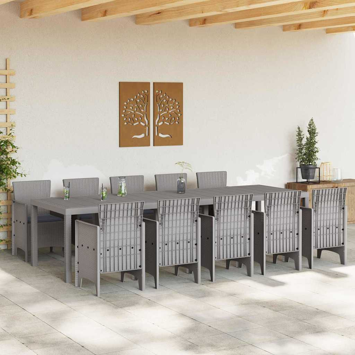 Essgruppe im Freien mit einem langen Tisch, zehn grauen Stühlen, dekorativer Wandkunst und Pflanzen auf einer Terrasse.