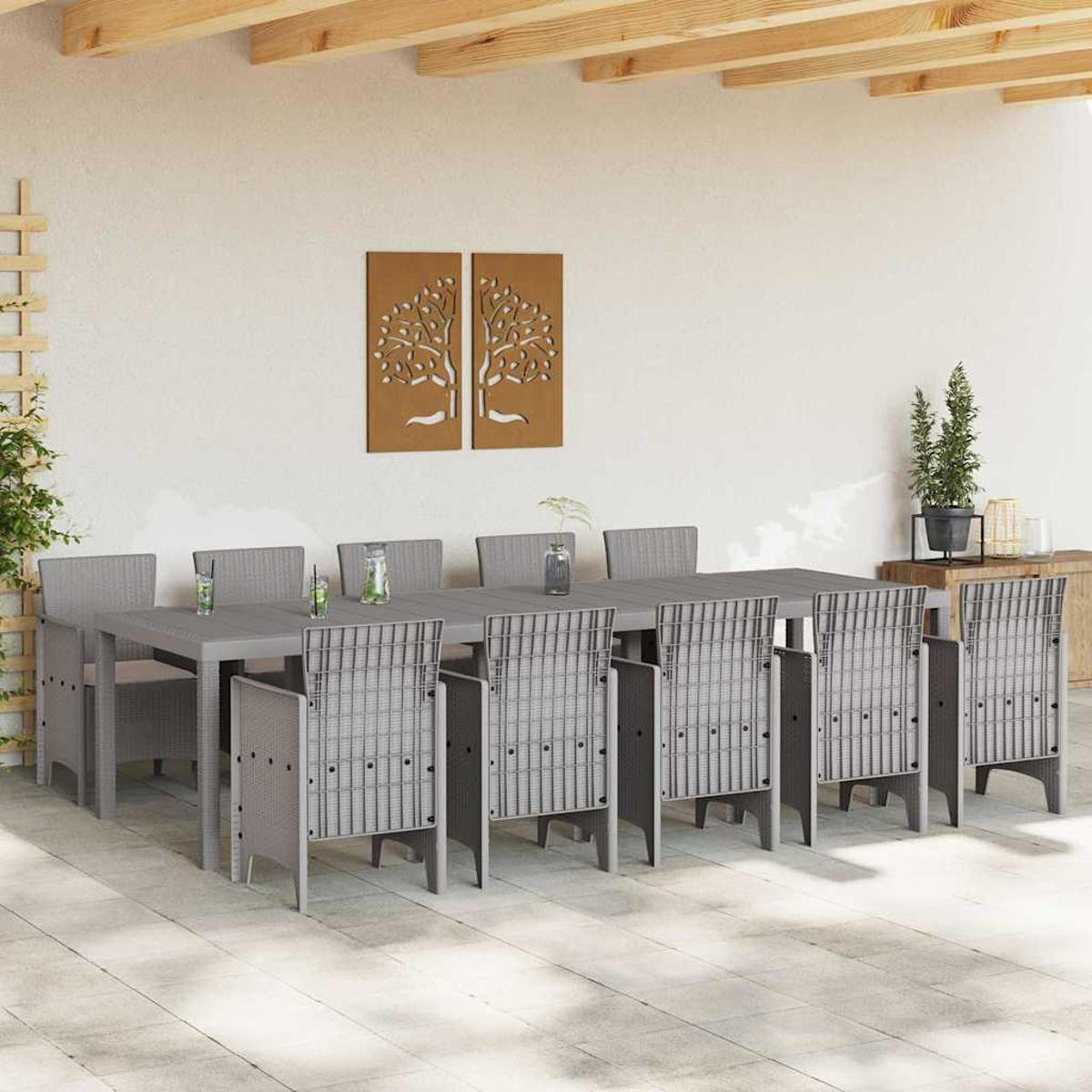 Essgruppe im Freien. Ein langer grauer Tisch mit Stühlen, Getränken und Pflanzen. Wandkunst mit Bäumen hängt darüber. Holzbalken darüber.