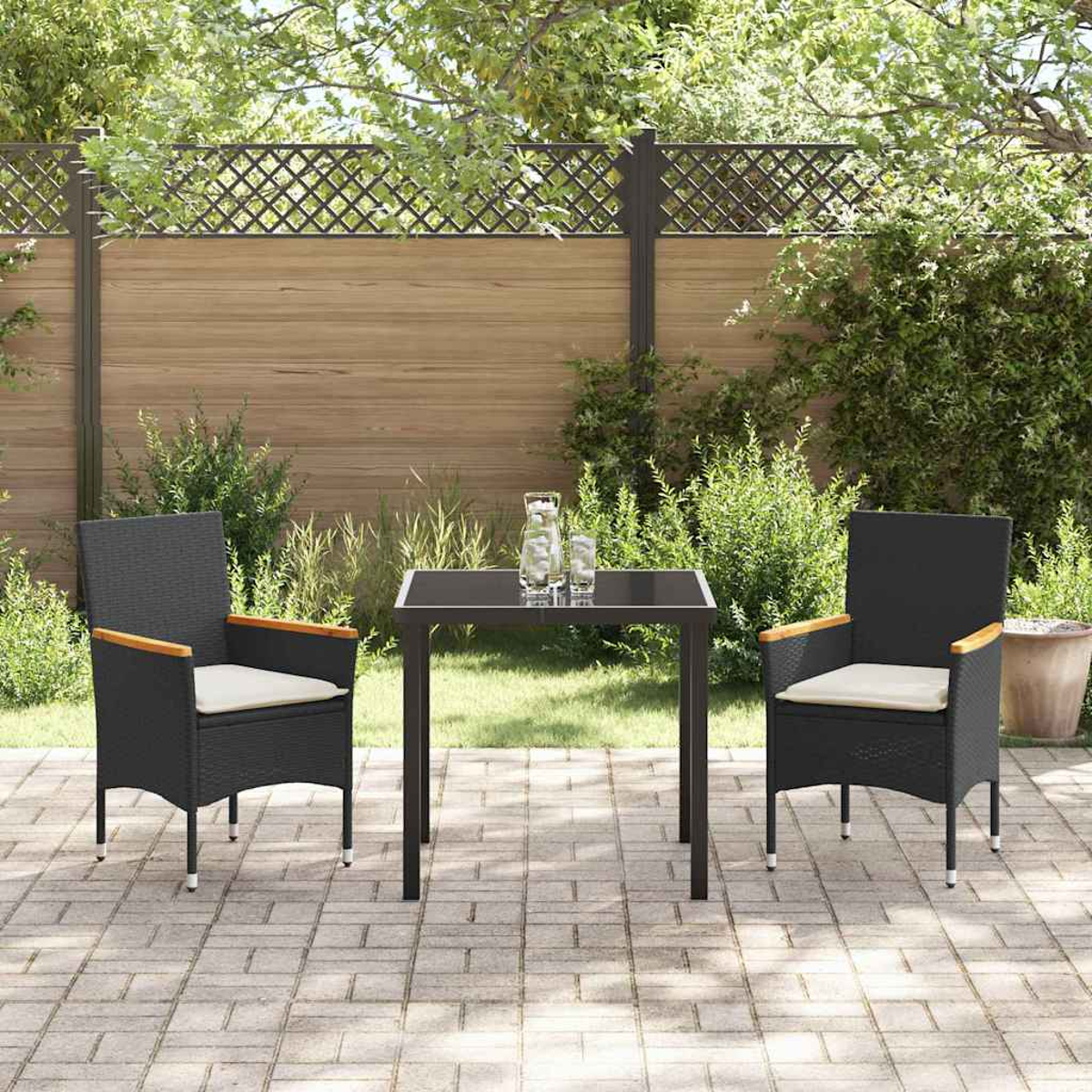 Ein Terrassenset mit zwei schwarzen Korbstühlen, einem kleinen Tisch und einem Holzzaun im Hintergrund, umgeben von Grün.
