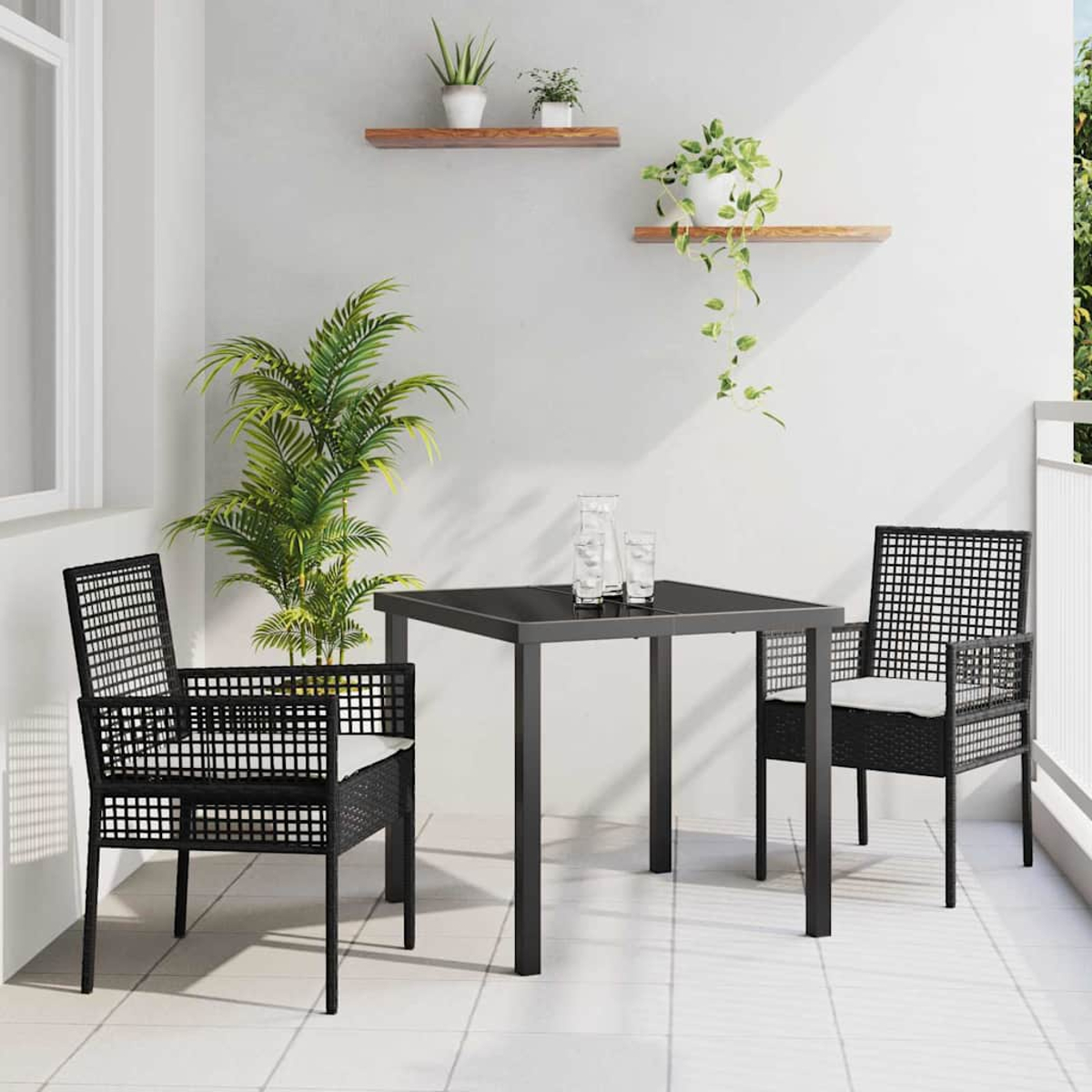 Scena di balcone con tavolo nero, due sedie, piante e due mensole con piante. Le sedie hanno cuscini bianchi.
