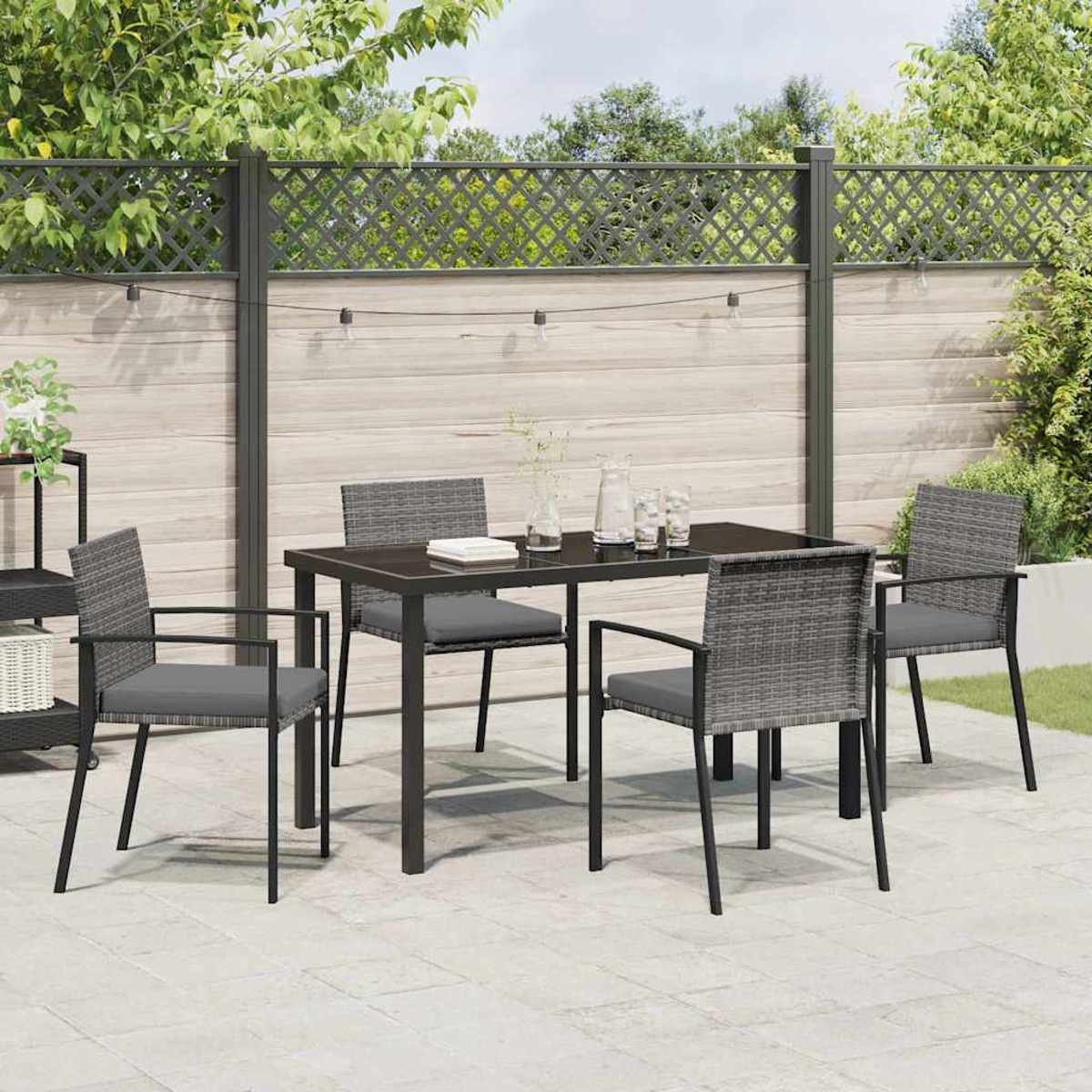 Ein Esszimmer-Set im Freien mit einem dunklen Tisch und grauen Stühlen steht auf einer Terrasse. Im Hintergrund sind ein Zaun und Grün.