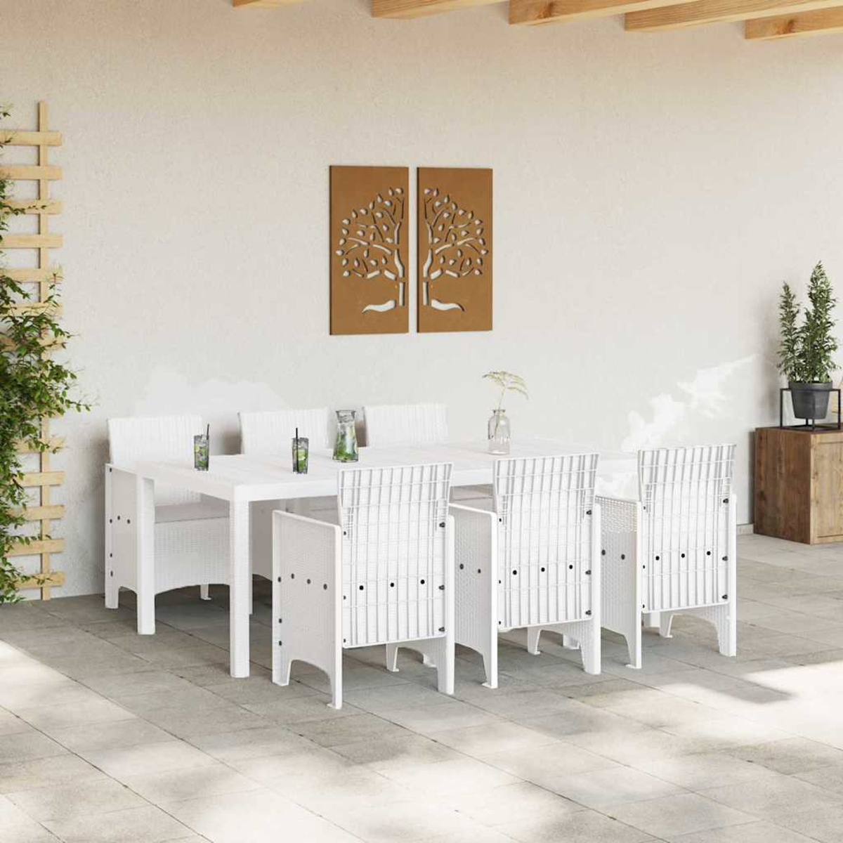 Essgruppe im Freien mit weißem Tisch und Stühlen. Braune Baumkunst an der Wand. Pflanzen und Getränke auf dem Tisch. Holzbalken oben.