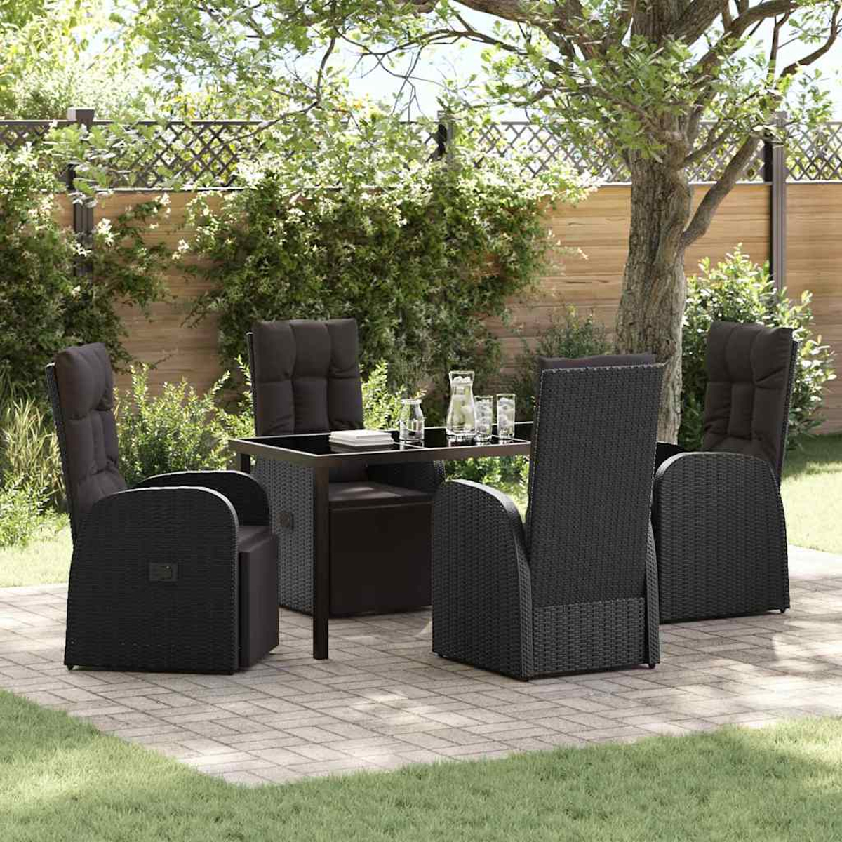Essgruppe im Freien: schwarze Korbstühle um einen Tisch auf einer Terrasse. Grünes Gras und Blätterwerk im Hintergrund.