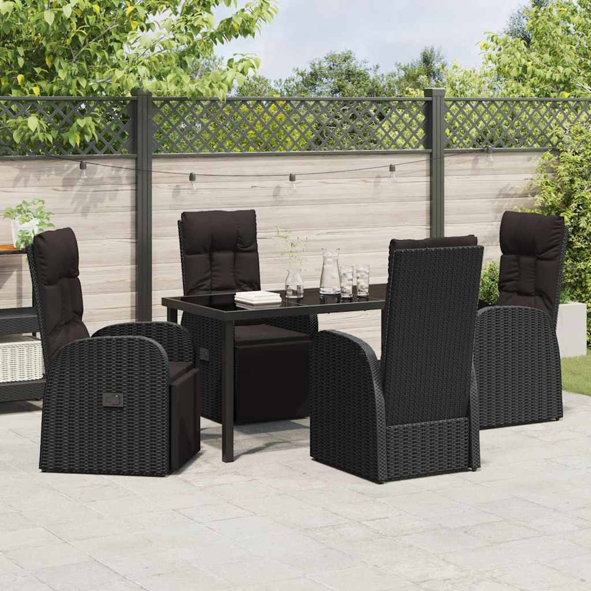 Essgruppe im Freien mit schwarzen Korbstühlen und einem Tisch auf einer Terrasse mit Zaun und Grün im Hintergrund.