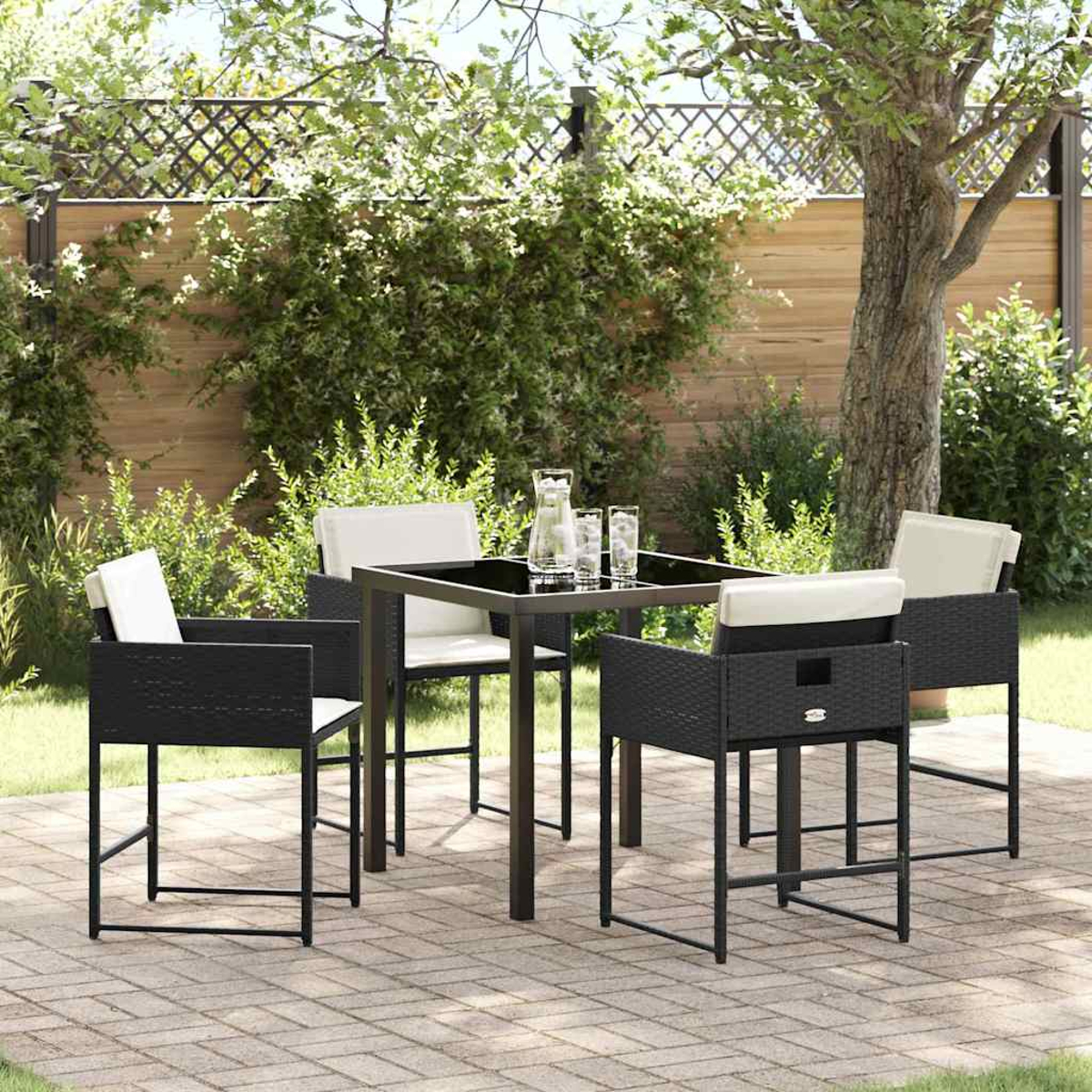 Terrassenset im Freien mit schwarzen Stühlen, einem Tisch und weißen Kissen. Gläser und ein Krug stehen auf dem Tisch. Grünes Laub im Hintergrund.