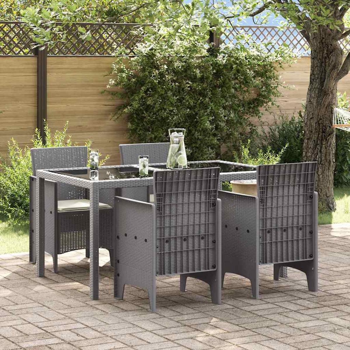 Essgruppe im Freien auf einer Terrasse. Grauer Tisch und Stühle, Getränke auf dem Tisch. Grünes Laub und Holzzaun im Hintergrund.