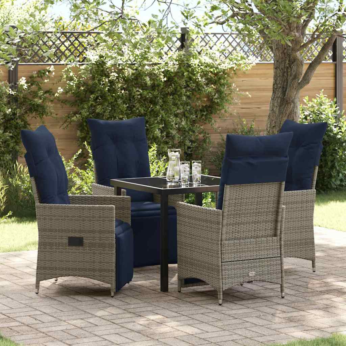 Vier Stühle und ein Tisch auf einer Terrasse. Stühle sind graues Korbgeflecht mit blauen Kissen. Tisch hat eine Glasplatte. Hintergrundeinstellung.