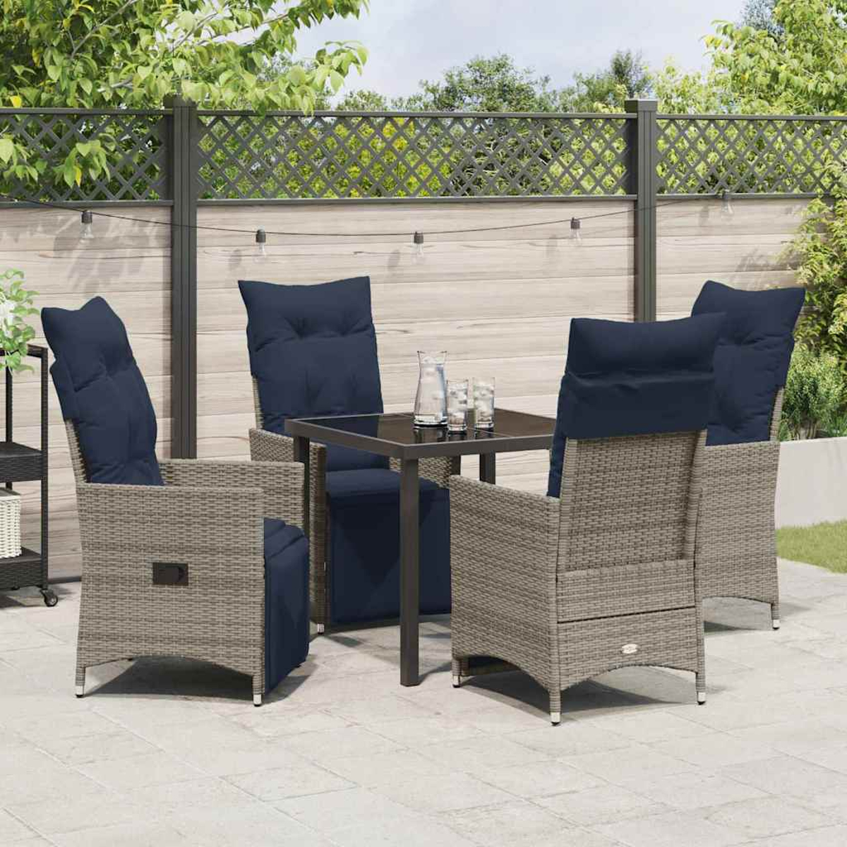 Terrassenset mit grauen Korbstühlen, marineblauen Kissen und einem quadratischen Tisch. Hintergrund ist ein Zaun und Grün.