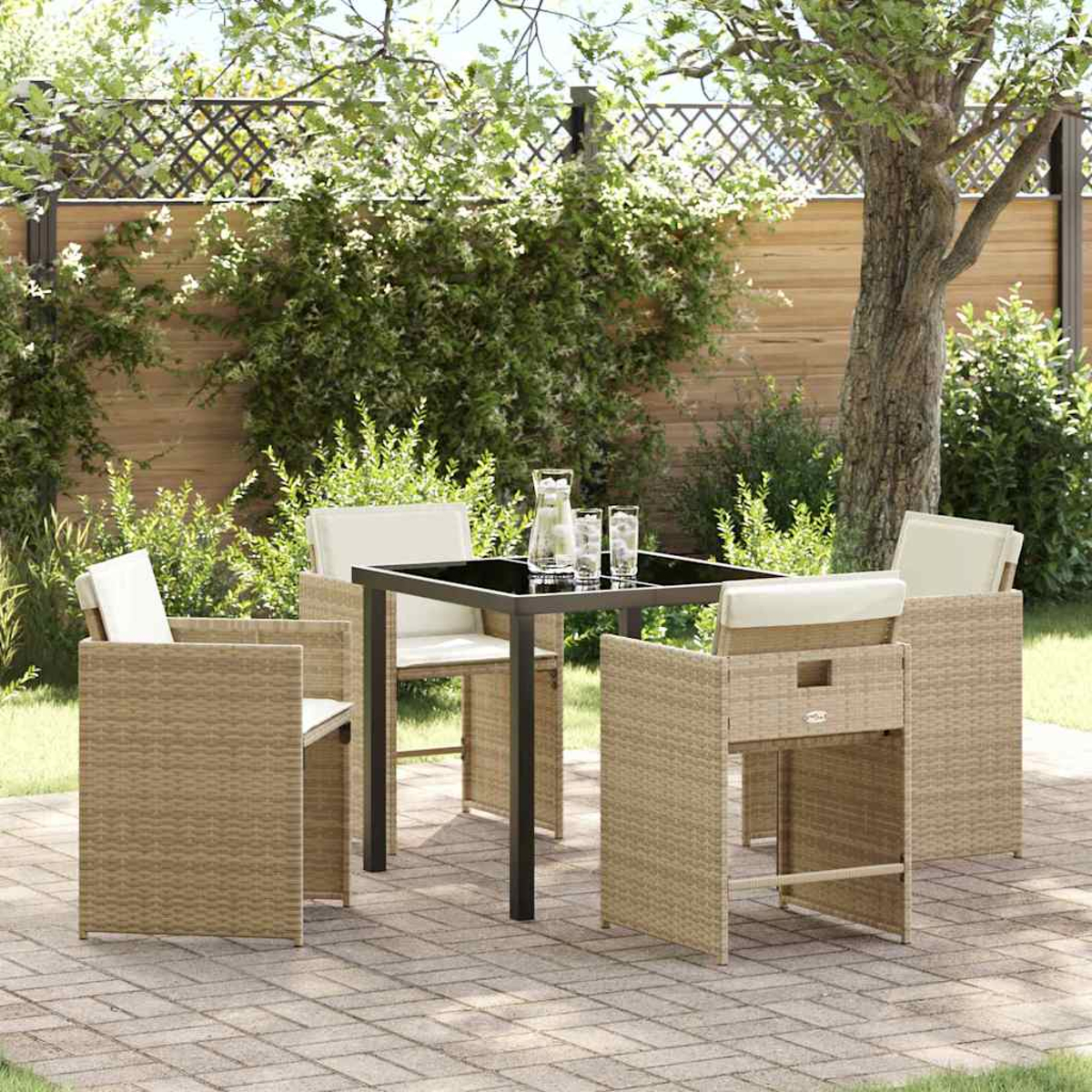 Terrassenset im Freien mit einem quadratischen schwarzen Tisch, vier Korbstühlen, einem Krug und Gläsern, umgeben von Grün.
