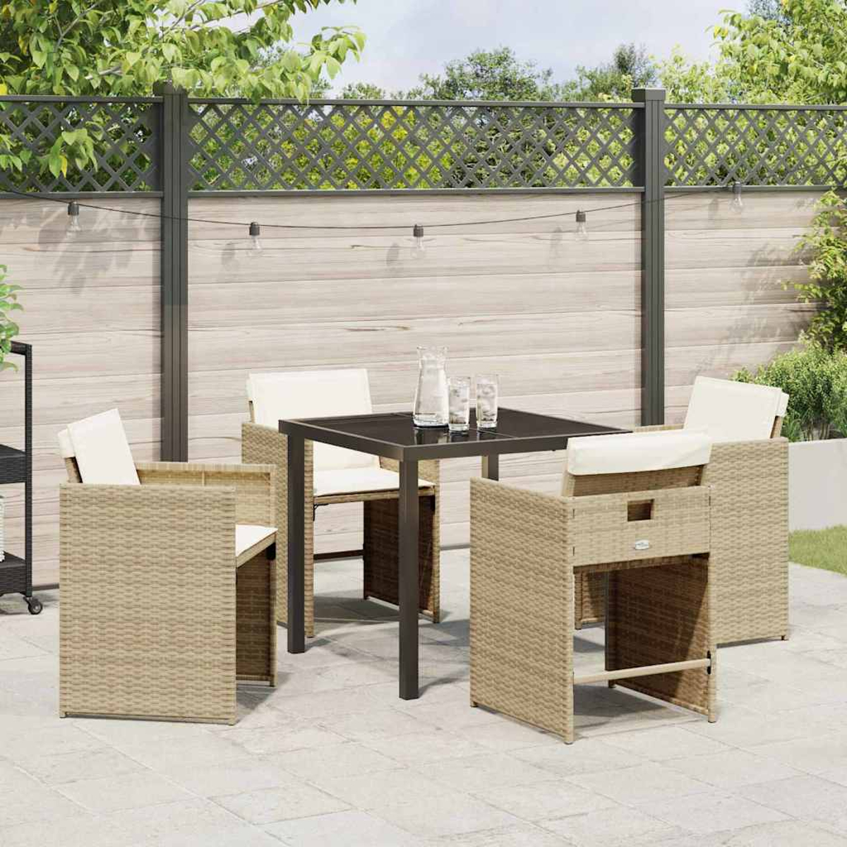 Garten-Terrassenset mit Tisch und Stühlen. Ein Zaun und Grün im Hintergrund. Tisch mit Gläsern und einem Krug.