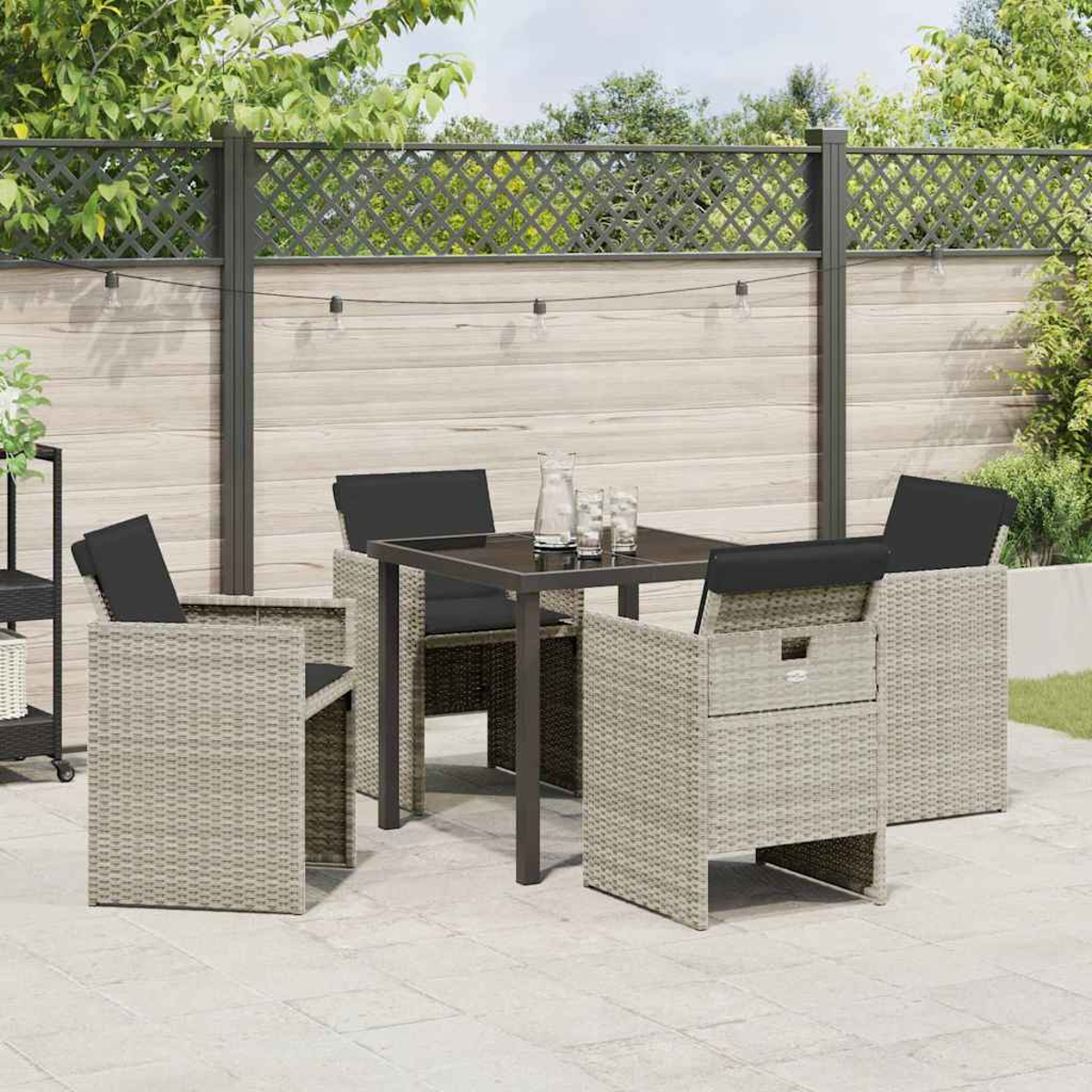 Set da patio esterno con tavolo e sedie. Il tavolo ha vetro e sedie nere con cuscini neri. Lo sfondo ha una recinzione.