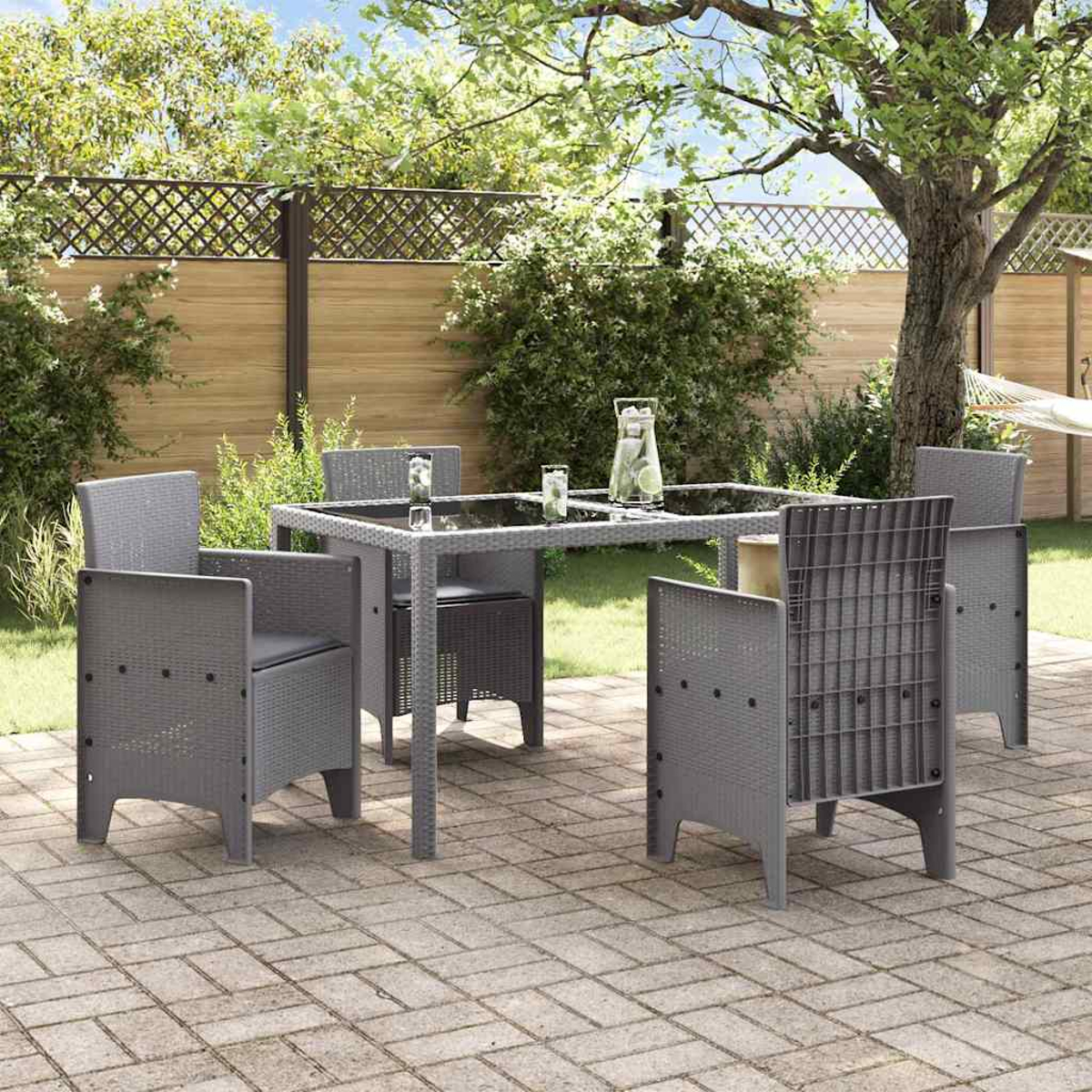 Szene im Freien mit einem grauen Tisch, Stühlen und Getränken auf einer Backstein-Terrasse. Bäume, ein Zaun und eine Hängematte im Hintergrund.
