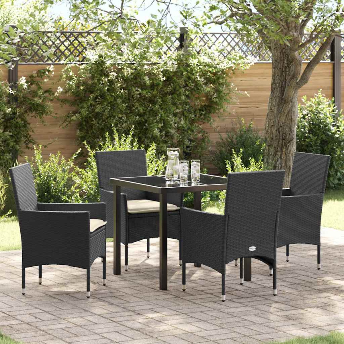 Essgruppe im Freien: schwarze Korbstühle und Tisch auf einer Terrasse, mit Grün und Holzzaun im Hintergrund.