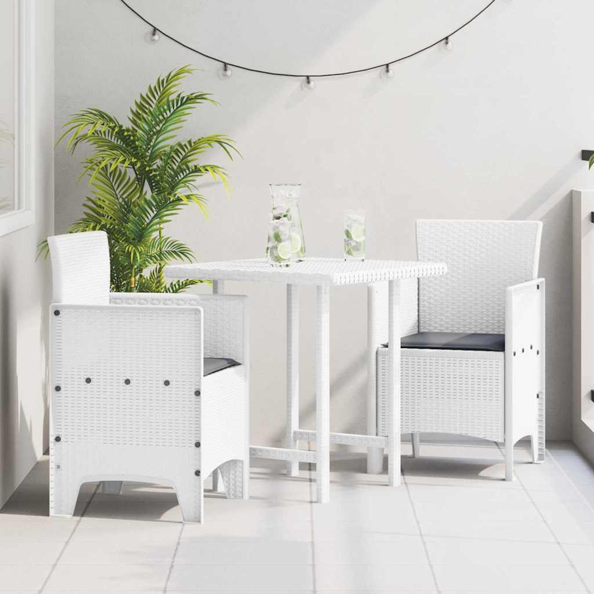 Weißes Terrassenset: Tisch, zwei Stühle. Palmenpflanze, Lichterkette und zwei Getränke mit Limettenscheiben. Weißer Fliesenboden, weiße Wände.
