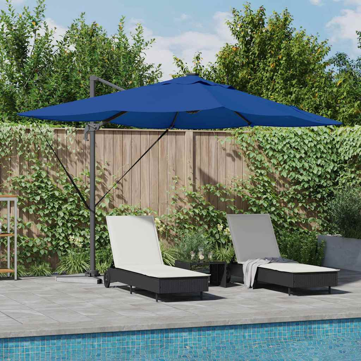 Zwei Liegestühle unter einem blauen Sonnenschirm am Pool. Im Hintergrund ein Holzzaun und üppiges Grün.