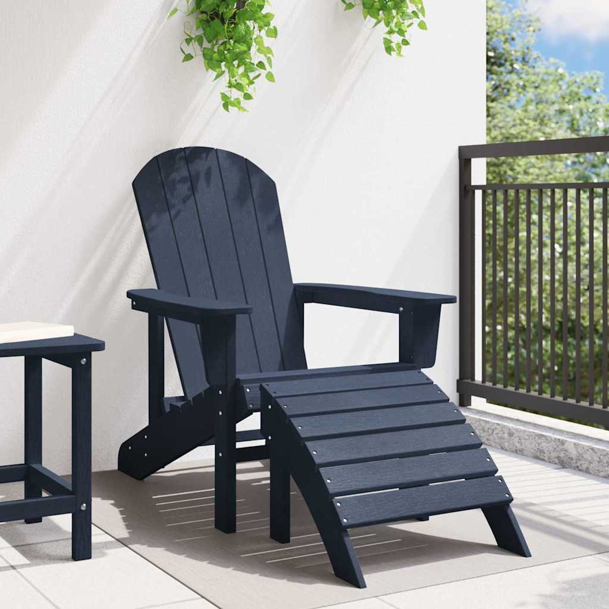 Dunkelblauer Adirondack-Stuhl mit Fußstütze auf einer Terrasse. Grüne Pflanzen hängen von oben. Links ein kleiner Tisch.