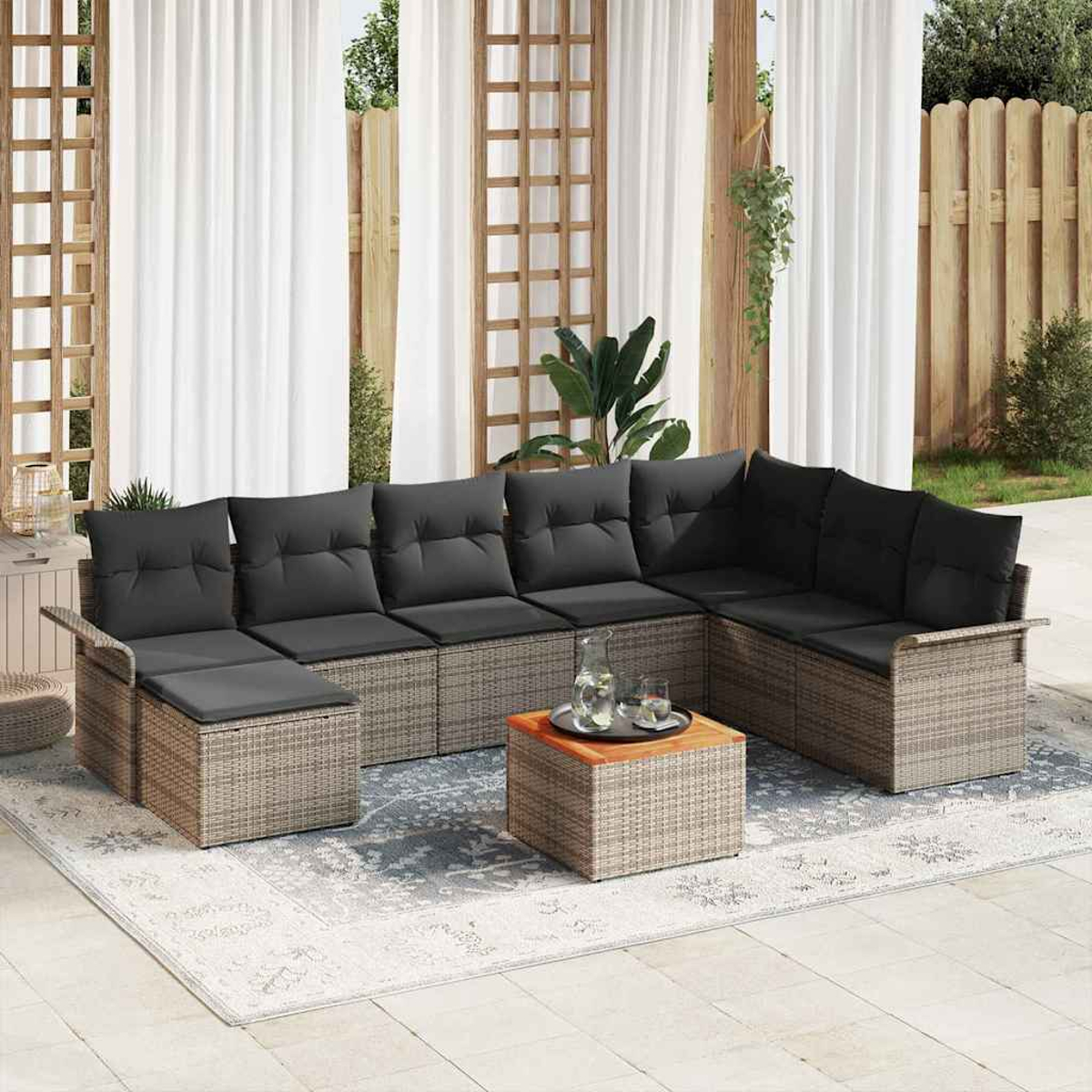 Outdoor-Ecksofa mit schwarzen Kissen, Couchtisch und Teppich. Hintergrund mit Vorhängen, Holzzaun und Pflanzen.