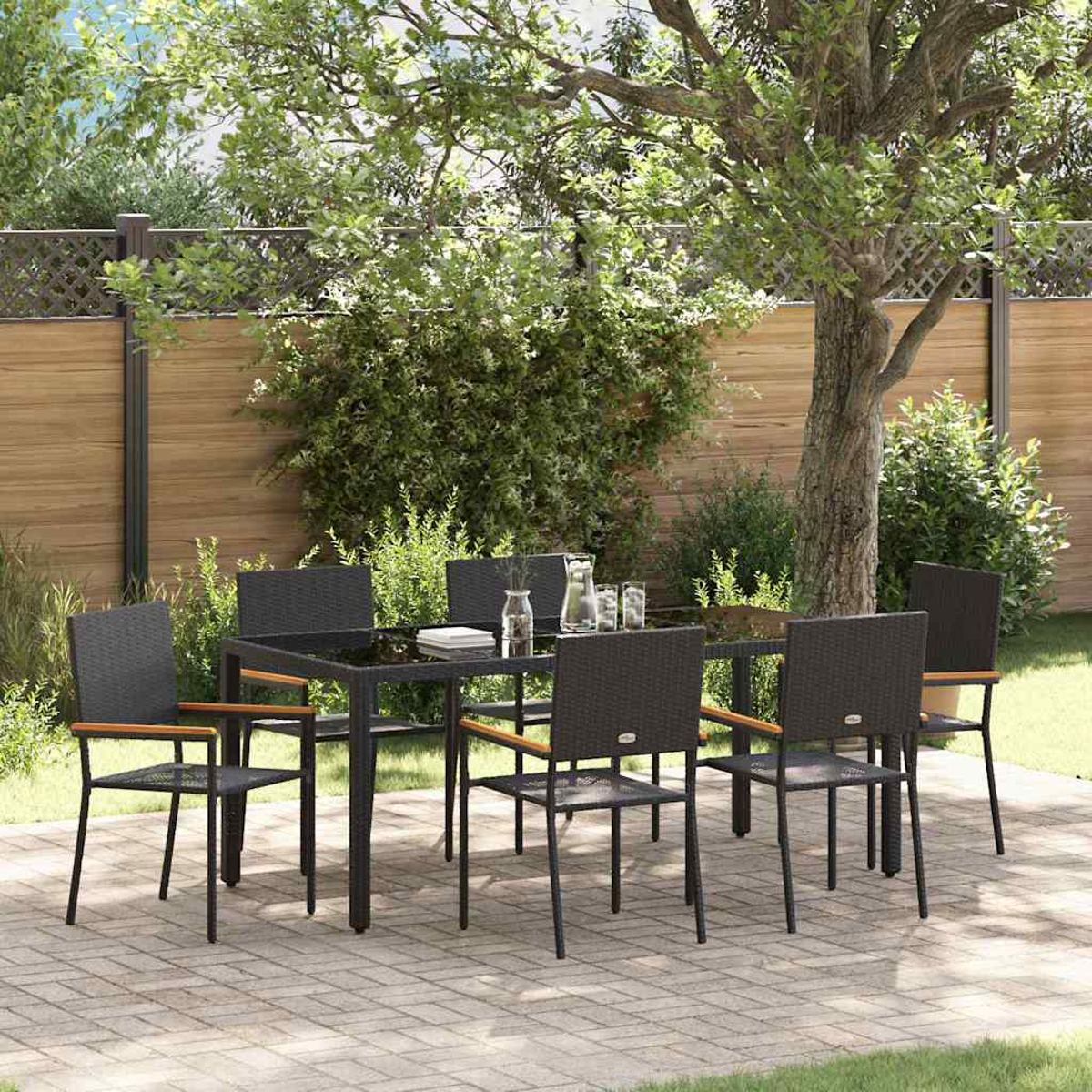 Garten-Essgruppe mit schwarzem Tisch und Stühlen auf einer Backstein-Terrasse. Ein Baum und Holzzaun sind im Hintergrund.