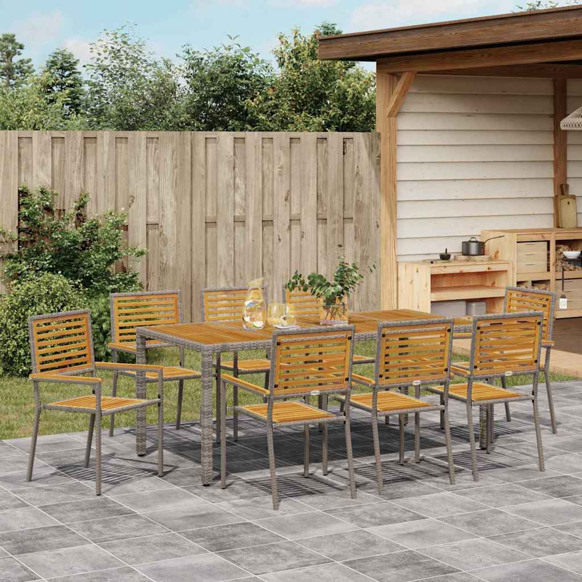 Essgruppe im Freien mit Holztisch und Stühlen auf einer Terrasse. Im Hintergrund ein Holzzaun und ein kleiner Unterstand.