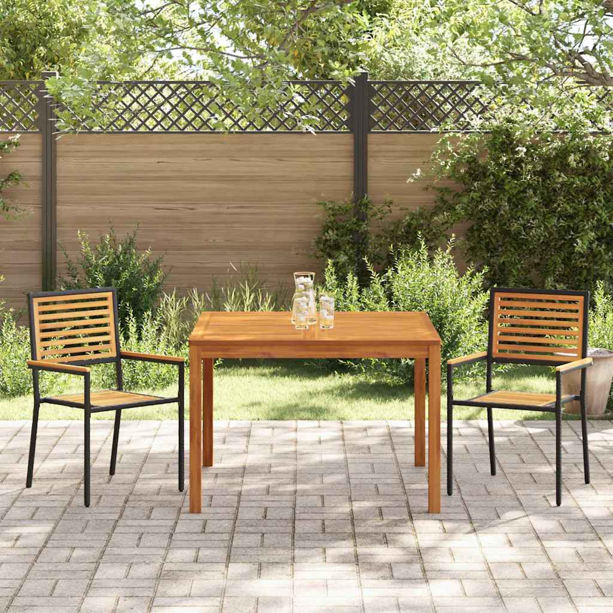 Escena al aire libre: mesa y sillas de madera en un patio. Una valla de madera en el fondo. Se ven arbustos y árboles verdes.