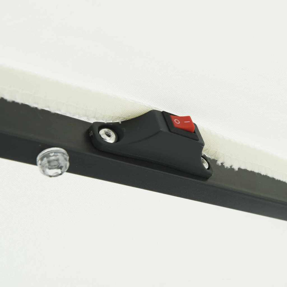 Primo piano di una struttura nera con un interruttore rosso. È visibile una piccola luce trasparente. Tessuto bianco sullo sfondo.